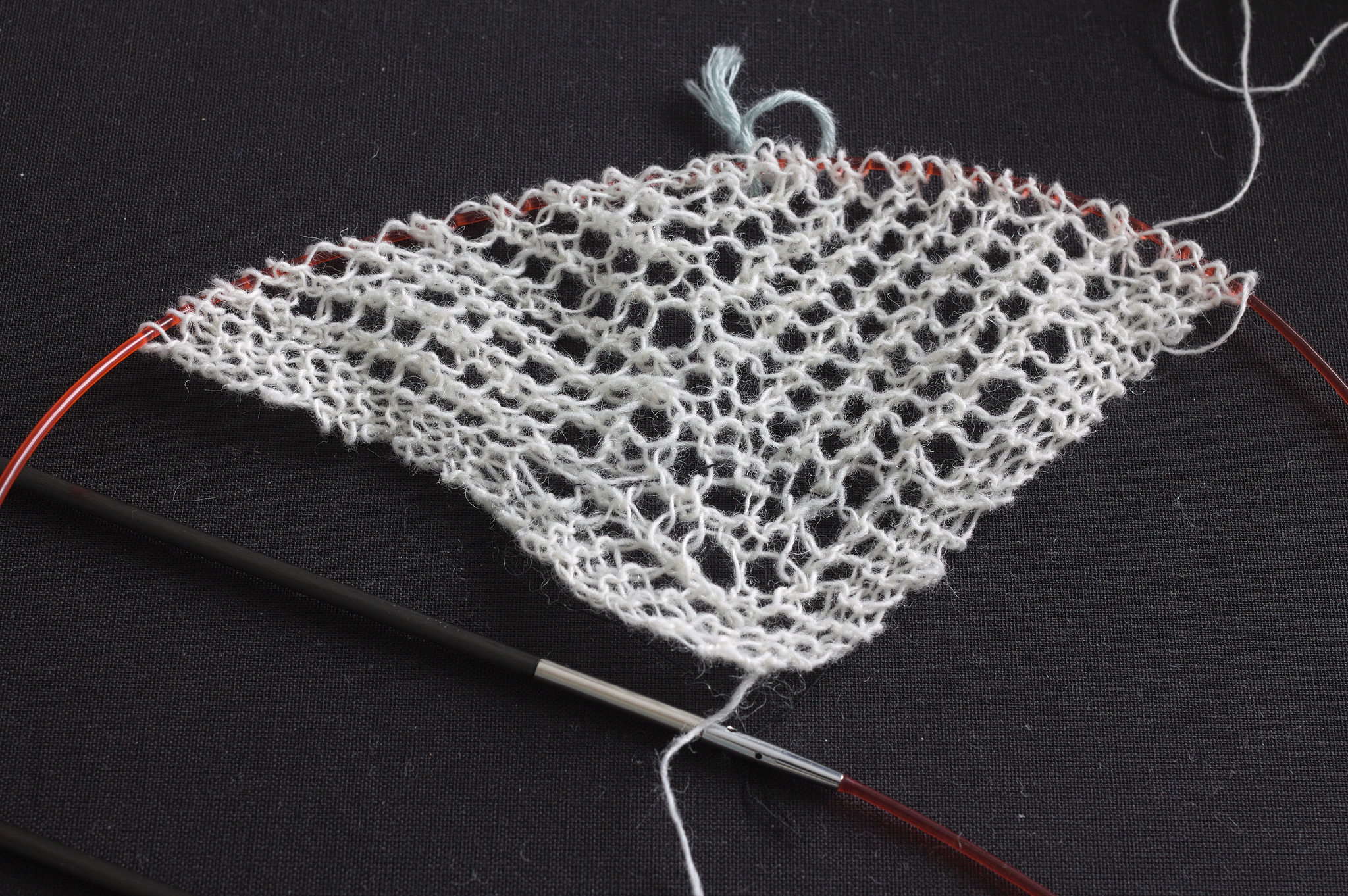 The beginning of a shawl in very thin white yarn, still on a circular needle with a stitch marker near the center stitch.